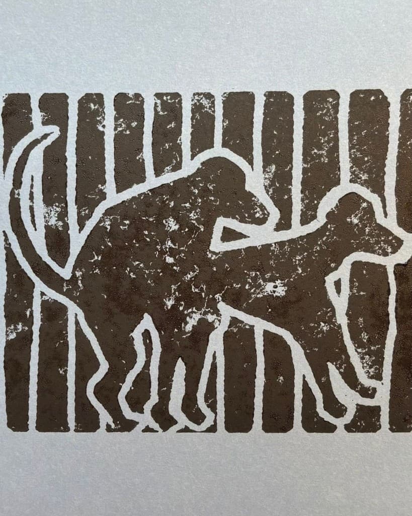 Linocut relief print of a dog in dark brown on silvery-grey paper, the artwork of The Carousel Vol. 2 — Doggy Dogg Summer